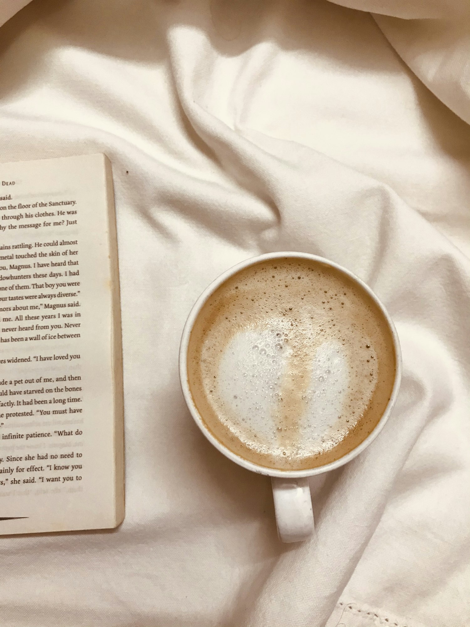 Une tasse de café posée sur du linge beige, à côté d'un livre ouvert